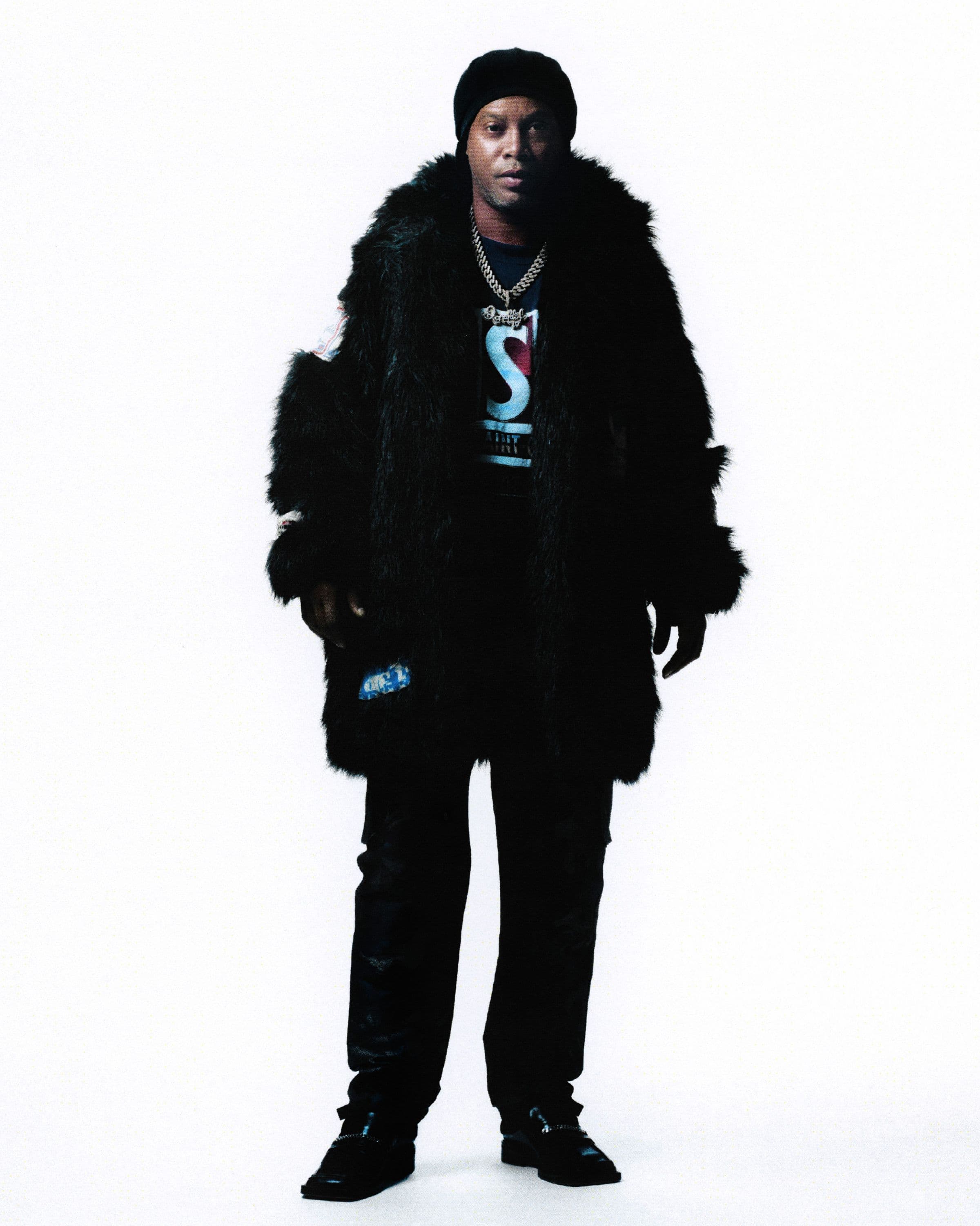 RONALDINHO wears a PSG tee from 1994, a custom diamond chain featuring the number 10, a jacket and mules by Martine Rose, and Dior pants.